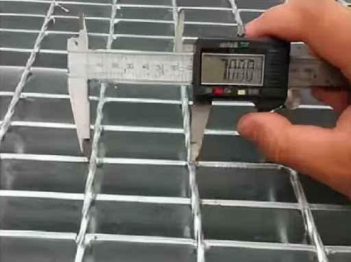Quality control technician measuring steel grating weld integrity with calipers to meet NAAMM and ASTM A123 standards.